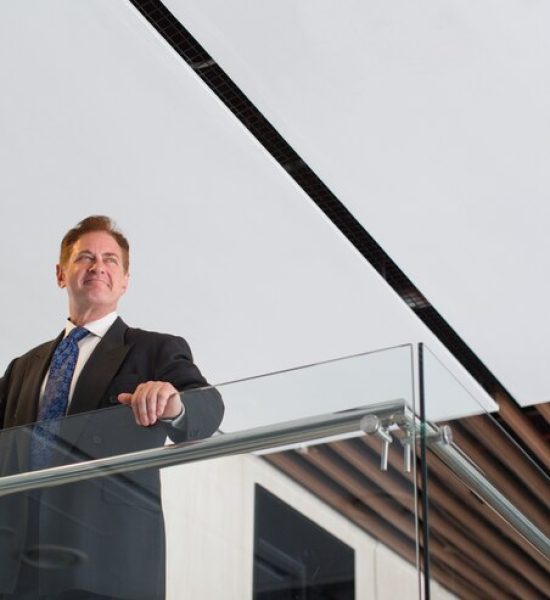 smiling-mature-businessman-standing-office-hall_1262-3105